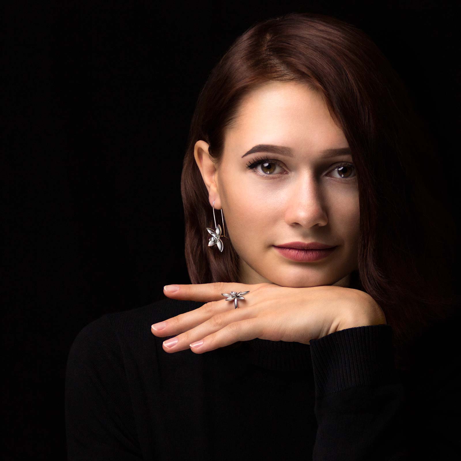 Девушка-модель на черном фоне в комплекте серебряных украшений "Лотос" из кольца и серег